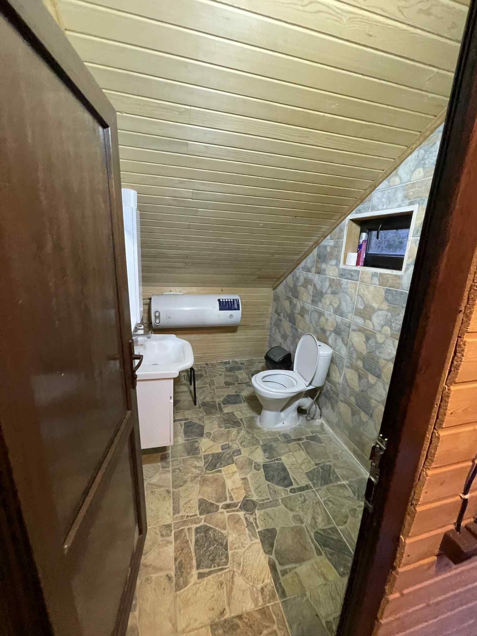 A small, sloped-roofed bathroom with a toilet, sink, and a built-in shower area.