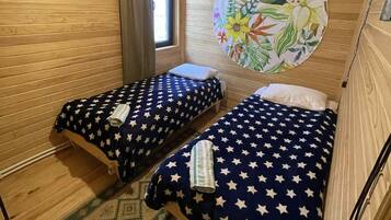 Une petite pièce agréable et chaleureuse, avec deux lits, une fenêtre avec des rideaux, un luminaire suspendu et un élément de décoration circulaire sur le mur.