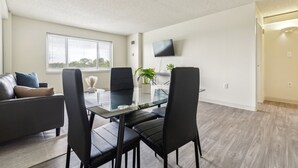 Un salon moderne avec une table à manger en verre, des chaises noires, un canapé en cuir et un téléviseur à écran plat fixé au mur.