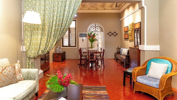 A living room with a sofa, a wicker chair, a dining table with chairs, and a coffee table with a vase of flowers. - Argus Residence (George Town)