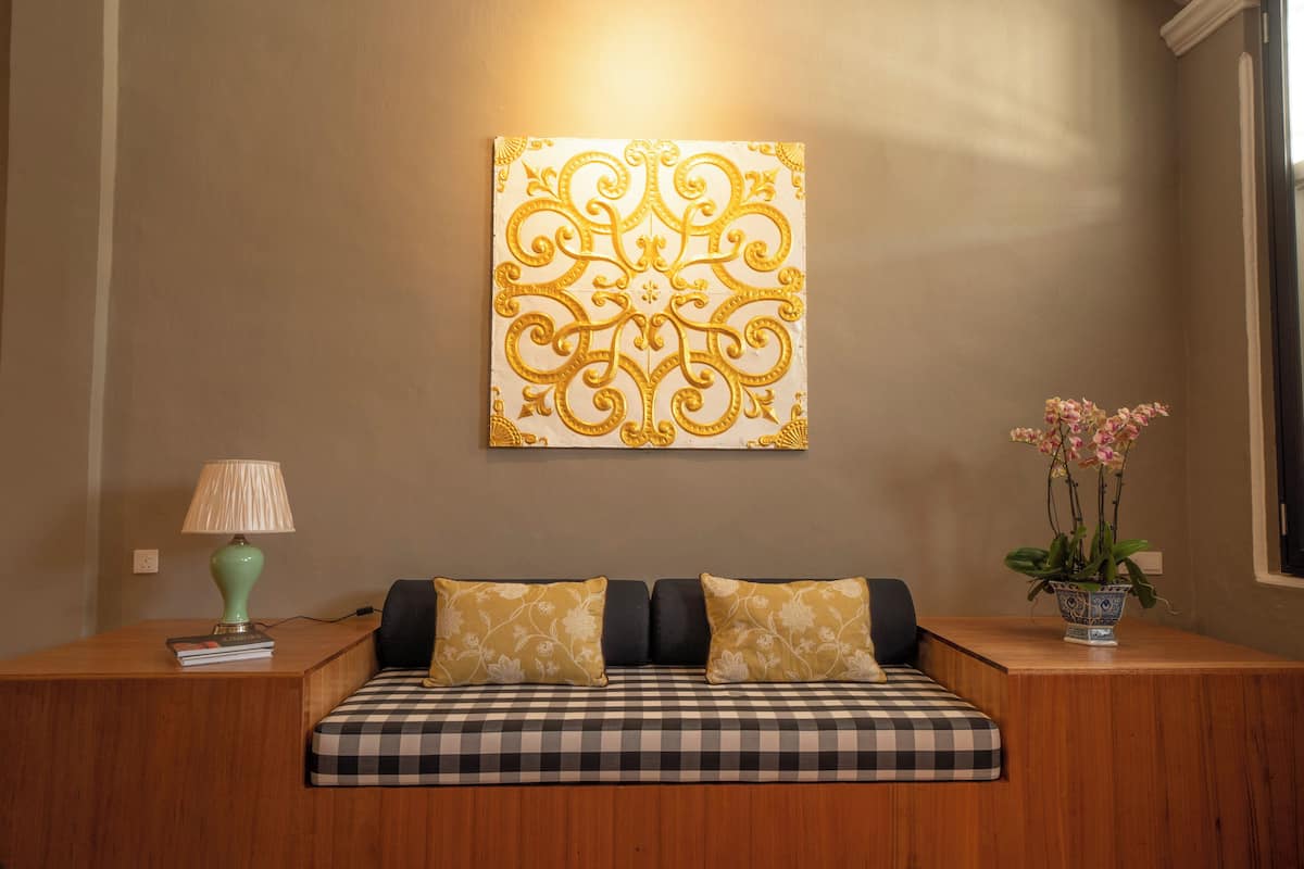 Una habitación con un sofá a cuadros, una lámpara, un adorno en la pared y un florero con flores.