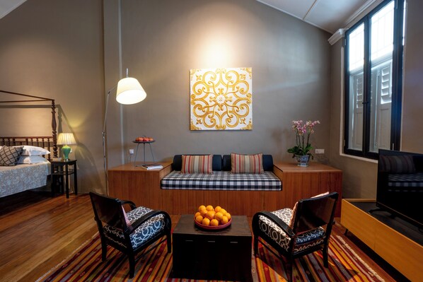 A modern living room with a sofa, two armchairs, a coffee table with oranges, a lamp, and a wall art piece. - Argus Residence (George Town)