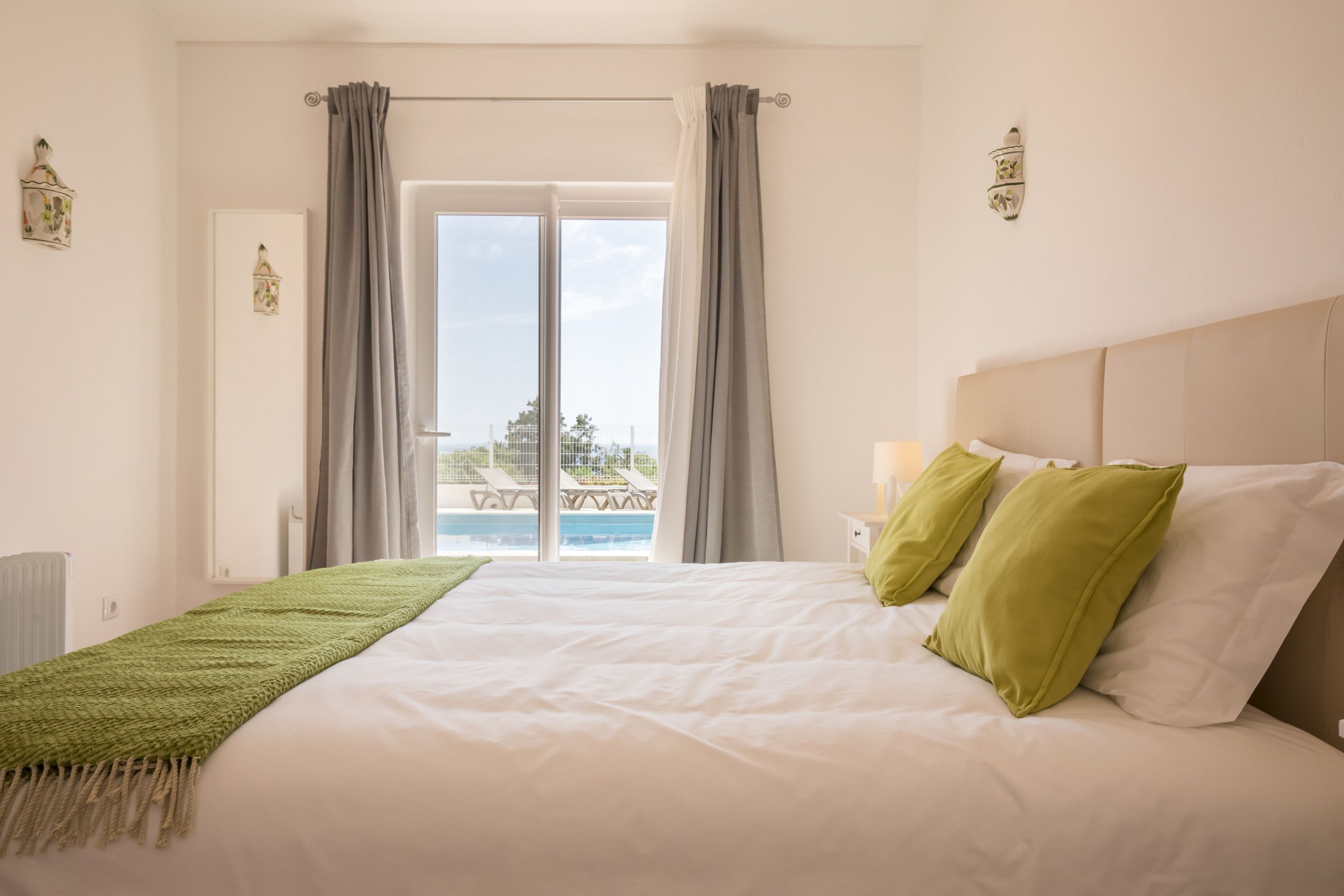 Un dormitorio con una cama grande, vistas a una piscina y sillas de descanso, y una ventana con cortinas.