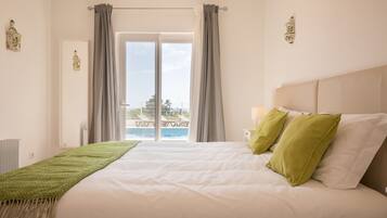 Un dormitorio con una cama grande, vistas a una piscina y sillas de descanso, y una ventana con cortinas.