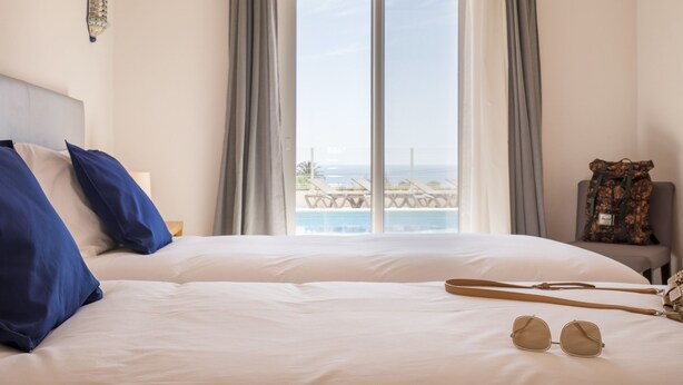 Een hotelkamer met een groot bed, uitzicht op de oceaan en een stoel met een bloemenprint.