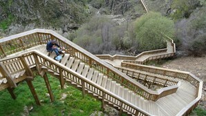 Un escalier en bois descendant une zone montagneuse, avec une personne assise sur les marches.