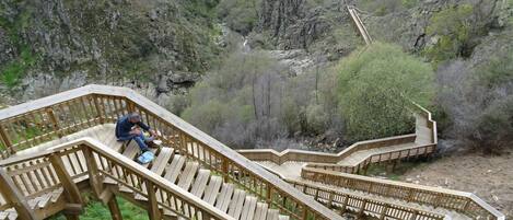Una escalera de madera que desciende por una zona montañosa, con una persona sentada en los escalones.
