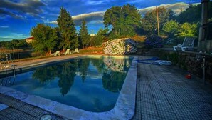 Une piscine dotée d’une terrasse carrelée, entourée d’arbres et bordée d’une structure en pierre.