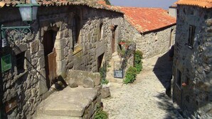Une ruelle étroite pavée, bordée de bâtiments en pierre aux toits recouverts de tuiles rouges, et surmontée d’un réverbère.