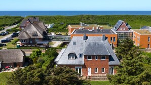 Ein Küstenwohngebiet mit einer Mischung aus traditioneller und moderner Architektur, darunter ein Haus mit Strohdach und ein Backsteinhaus mit großen Fenstern.