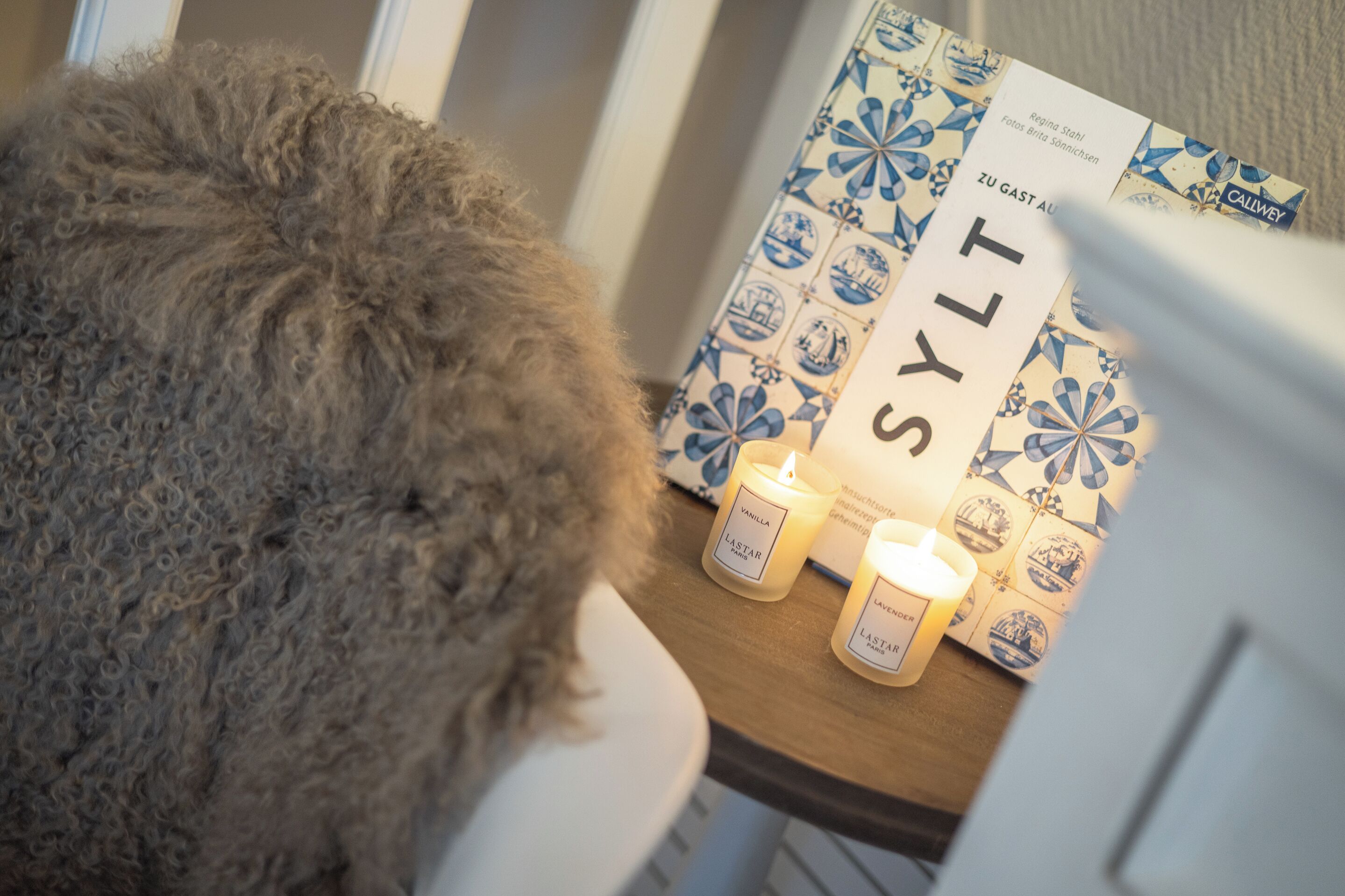 A cozy room with a fluffy rug, a candle, and a book titled 'SYLT' on a wooden table.