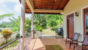 A covered porch with a tiled floor, a wooden bench, and a view of a lush garden and parked car. - 4-bedroom Green Oasis in Kandy (Kandy)