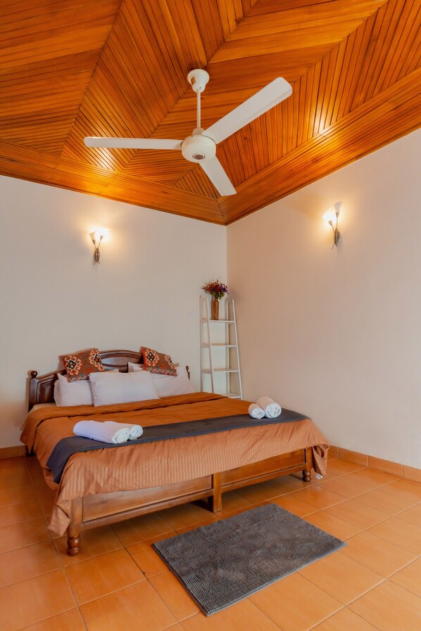 A bedroom with a wooden ceiling, a bed with a brown bedspread, a white ceiling fan, and a small white ladder against the wall.
