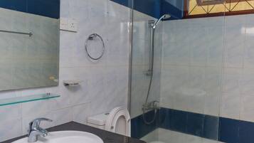 Et badeværelse med et hvidt håndvask, toilet, glas brusekabine og et spejl.