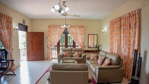 A living room with a sofa, armchairs, a coffee table, and a TV. There is a ceiling fan, a door, and curtains. - 4-bedroom Green Oasis in Kandy (Kandy)