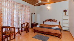 A bedroom with a wooden ceiling, a bed with an orange bedspread, a wooden chair, a small table, a mirror, and a white shelf with a vase of flowers. - 4-bedroom Green Oasis in Kandy (Kandy)