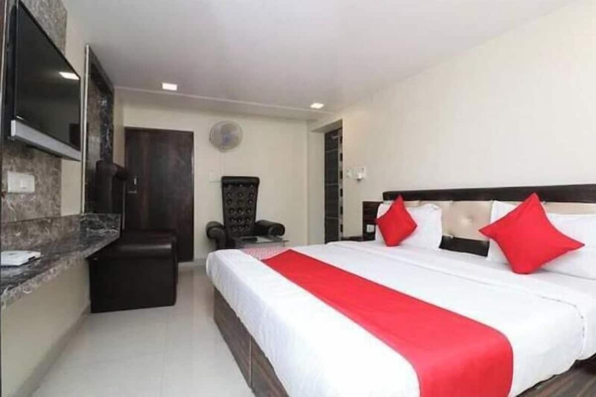 A hotel room with a large bed, a TV mounted on the wall, a desk, and a chair.