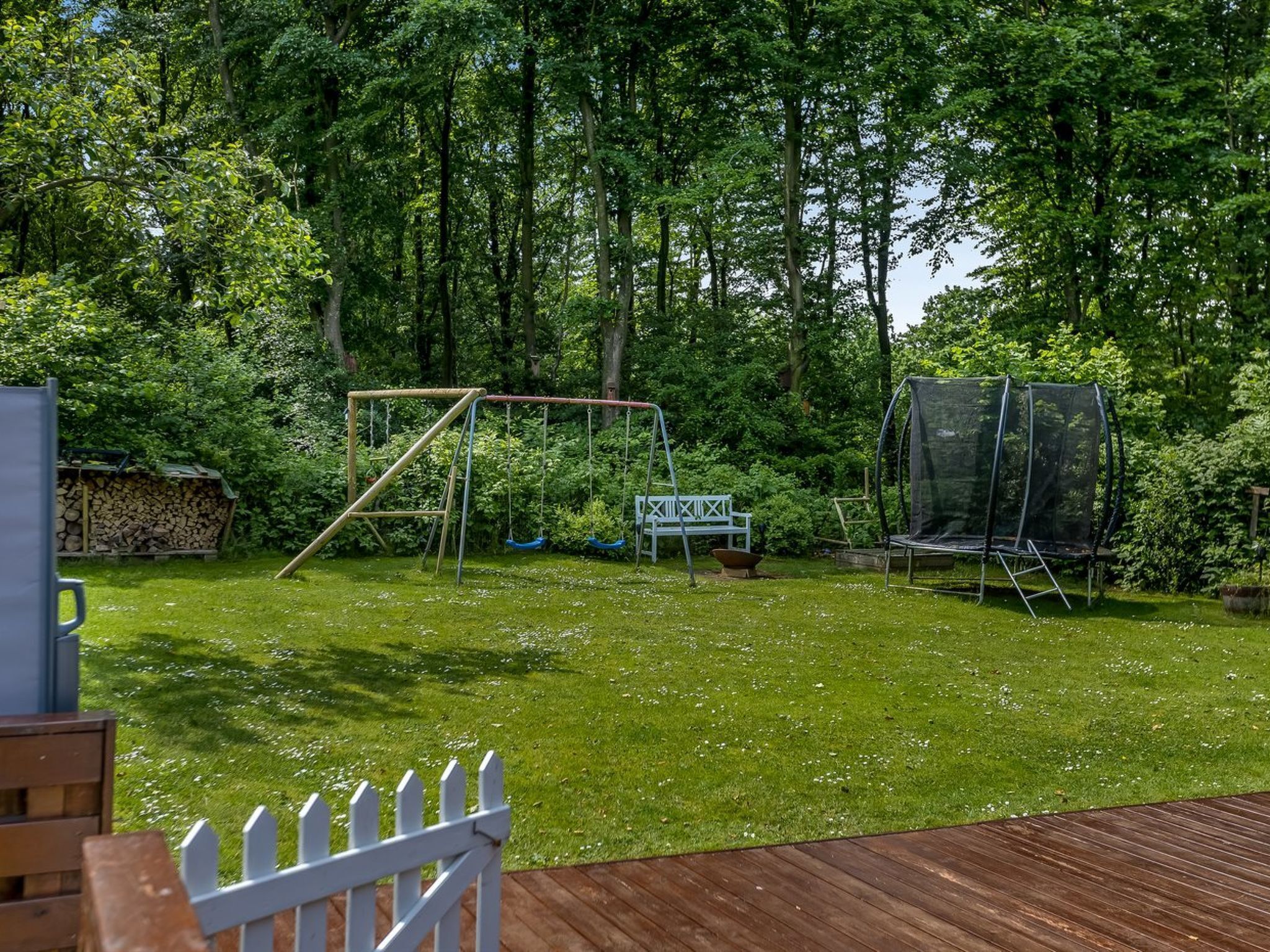 Un jardin avec une balançoire, un trampoline et une clôture blanche.