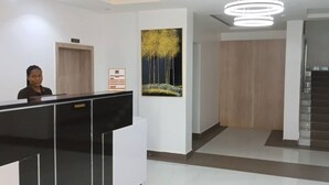 A reception area with a black reception desk, a framed artwork on the wall, and a staircase to the right. - Slavan Suites & Apartments (Owerri)