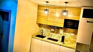 A modern kitchen with a granite countertop, stainless steel sink, and built-in appliances including a microwave and refrigerator. - Slavan Suites & Apartments (Owerri)