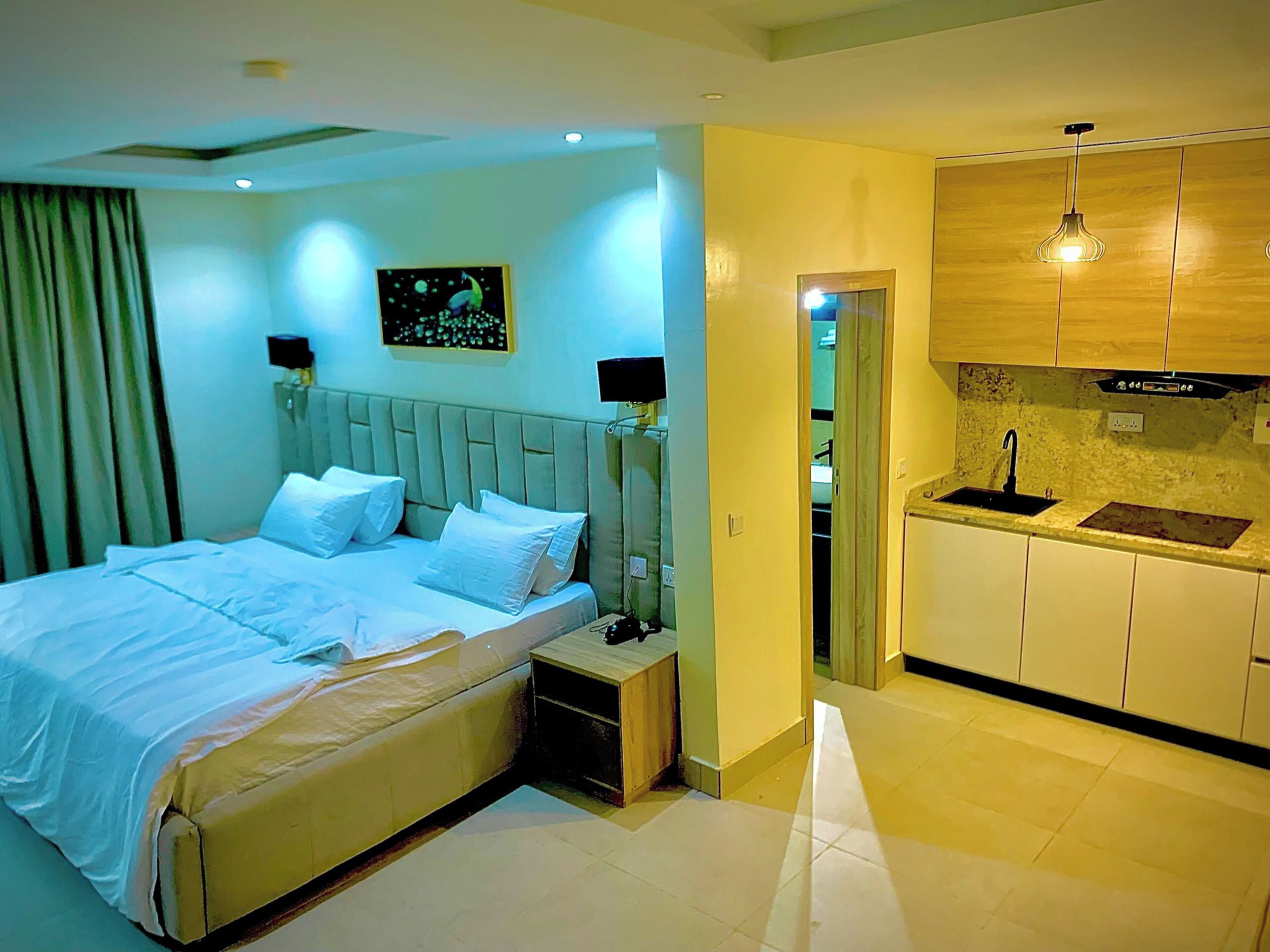 Un dormitorio con una cama, mesitas de noche y un pequeño armario. Cuenta con una kitchenette con un lavamanos y armarios.