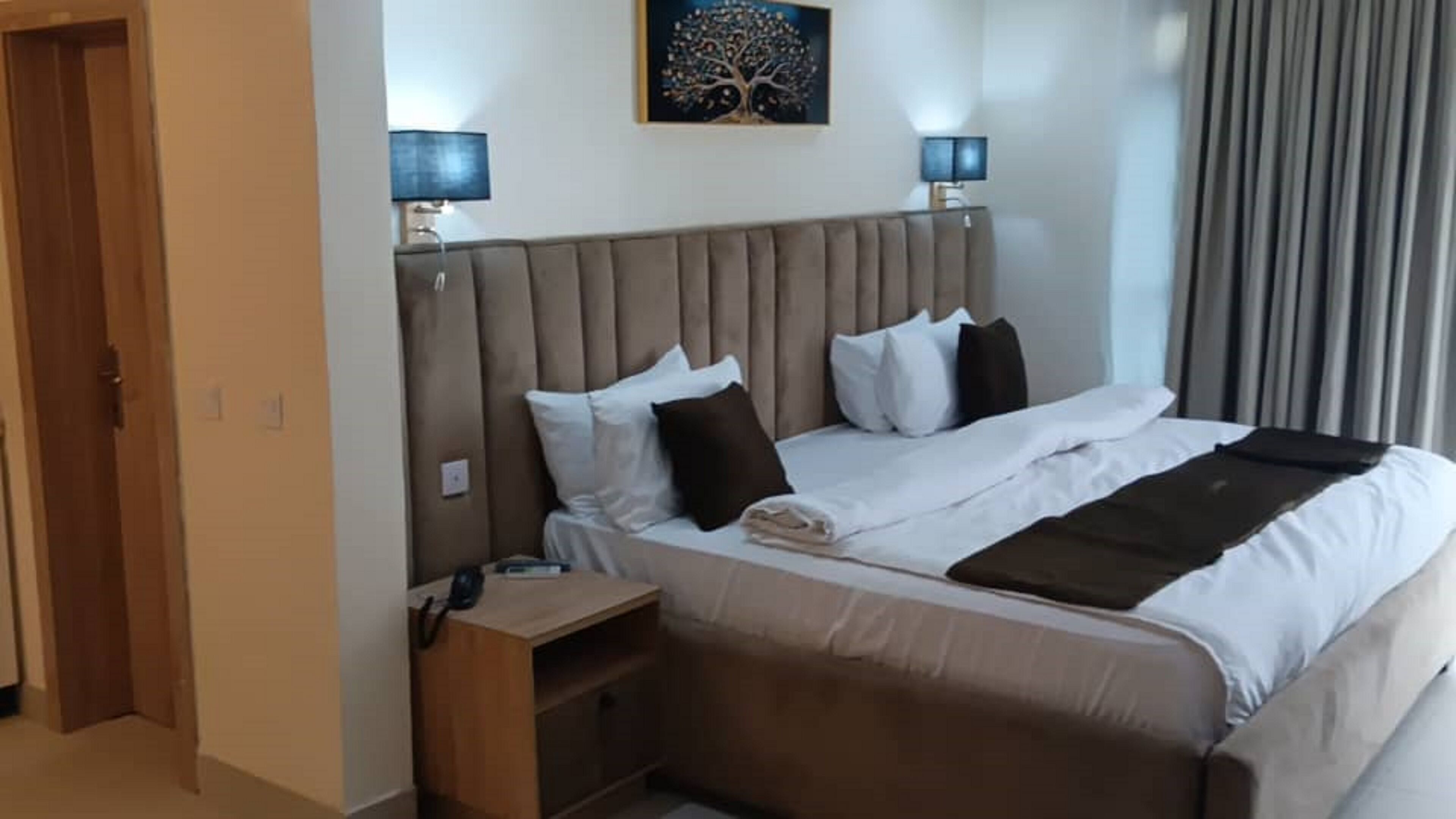 A hotel room with a large bed, two bedside lamps, a nightstand, and a painting on the wall.