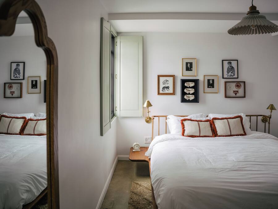 Una camera da letto con un grande specchio, un letto con biancheria da letto bianca e cuscini arancioni, un comodino con una lampada e quadri appesi alla parete.