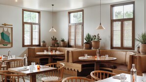 A cozy restaurant with wooden furniture, large windows with shutters, and potted plants. - The Landing Social House (Chattanooga)