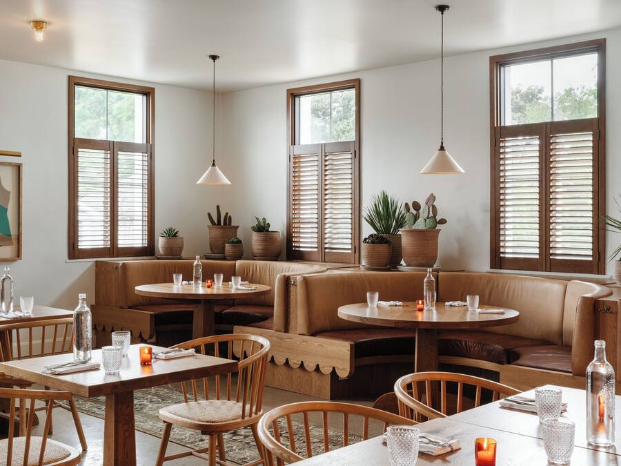 Un restaurant chaleureux, avec des meubles en bois, de grandes fenêtres équipées de volets et des plantes en pot.