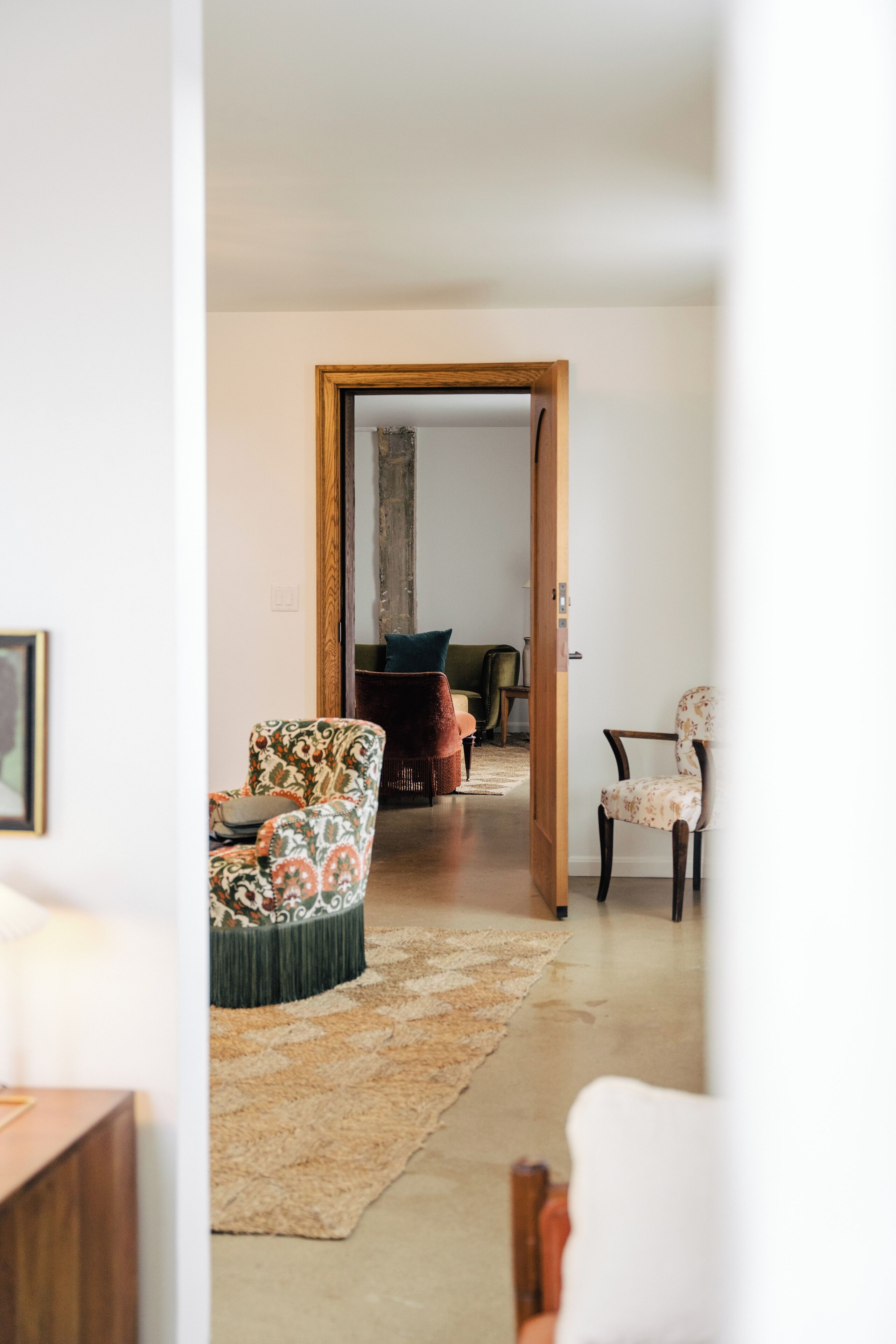 A living room with a patterned armchair, a wooden door leading to another room, and a green sofa.