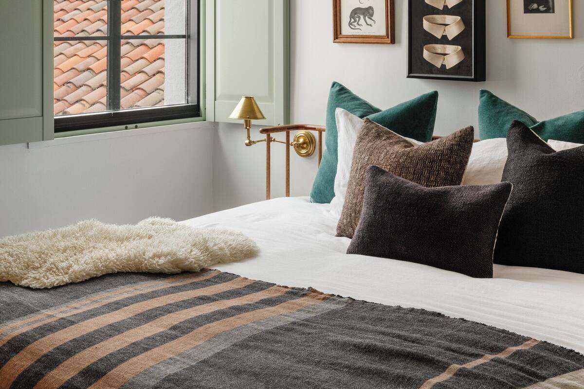 Un dormitorio con cama, almohadas, una ventana y decoración en la pared.