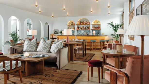 A spacious living area with a sofa, coffee table, and chairs. There is a bar area with shelves of bottles and a lamp. - The Landing Social House (Chattanooga)