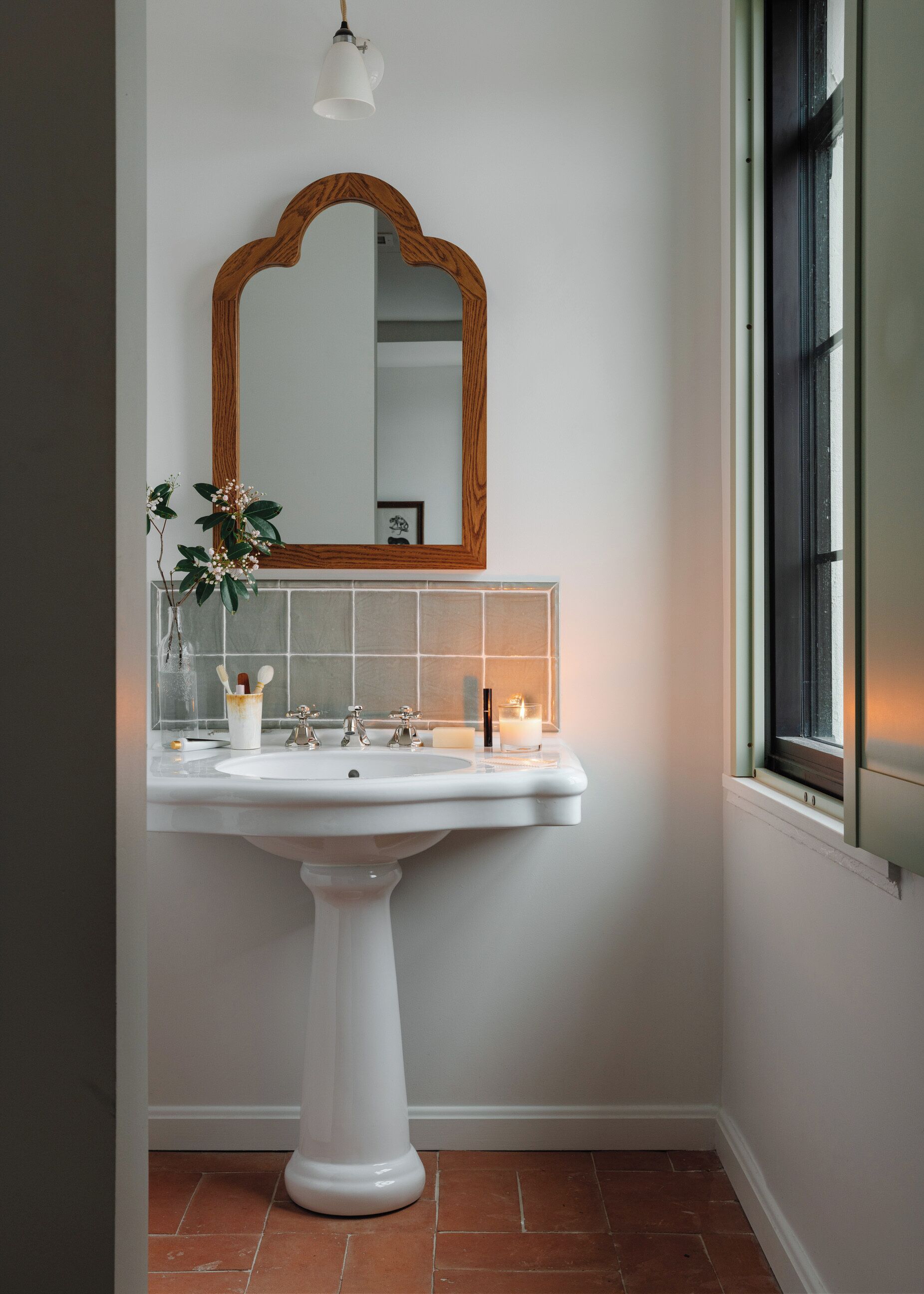 Un baño con lavamanos pedestal, espejo con marco de madera y ventana con vistas.