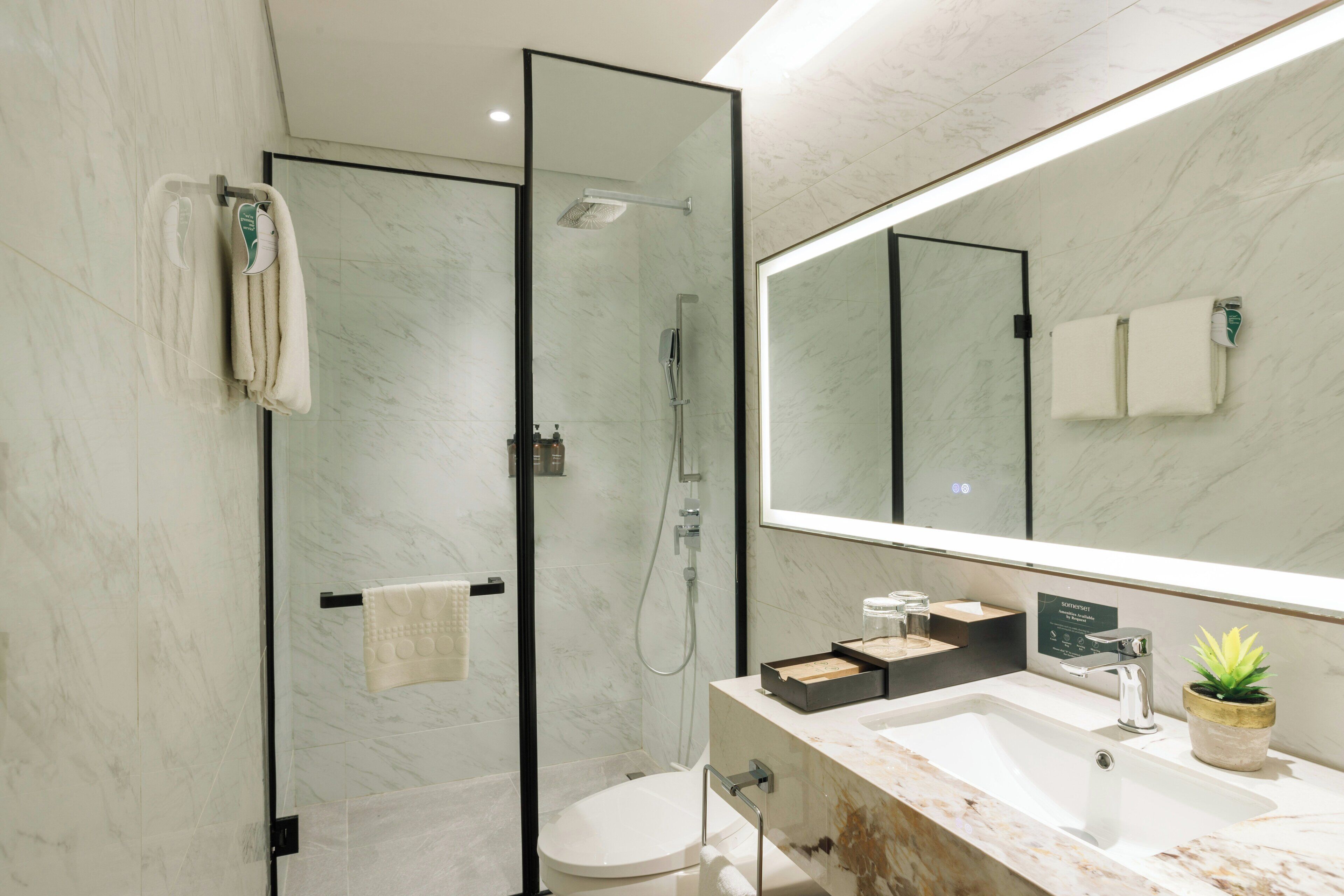 A modern bathroom with a glass-enclosed shower, a large mirror, and a marble countertop.