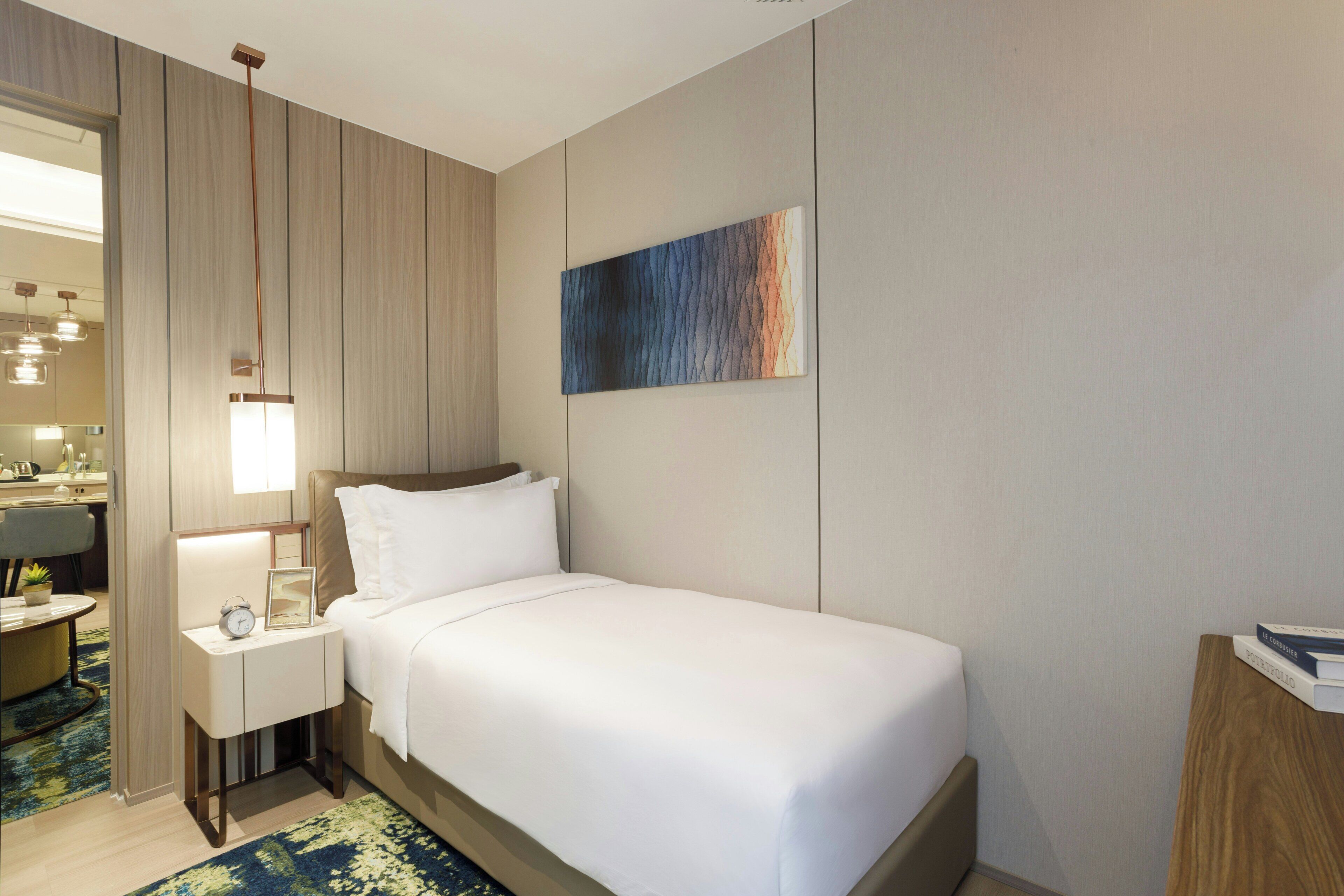 Ett hotellrum med en säng, ett nattduksbord, en lampa, konstverk och utsikt över badrummet.