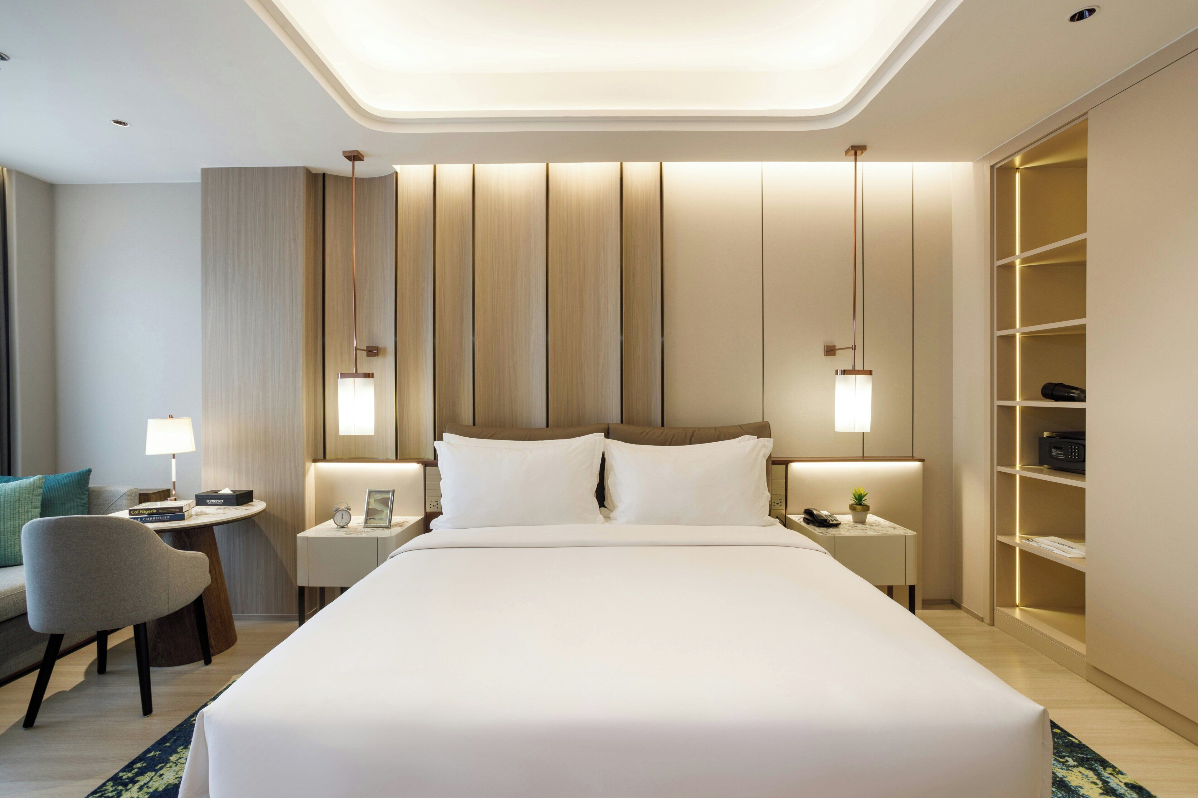 Une chambre d’hôtel moderne, dotée d’un grand lit, de tables de chevet, d’un bureau, d’une chaise et d’une armoire intégrée.