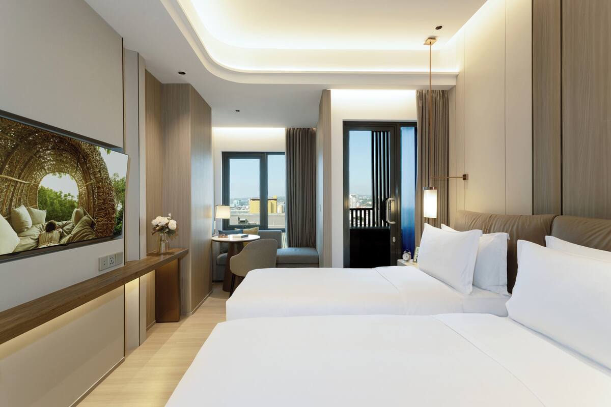 Une chambre d’hôtel moderne dotée d’un grand lit, d’un bureau, d’une chaise et offrant une vue sur la ville grâce à de grandes fenêtres.
