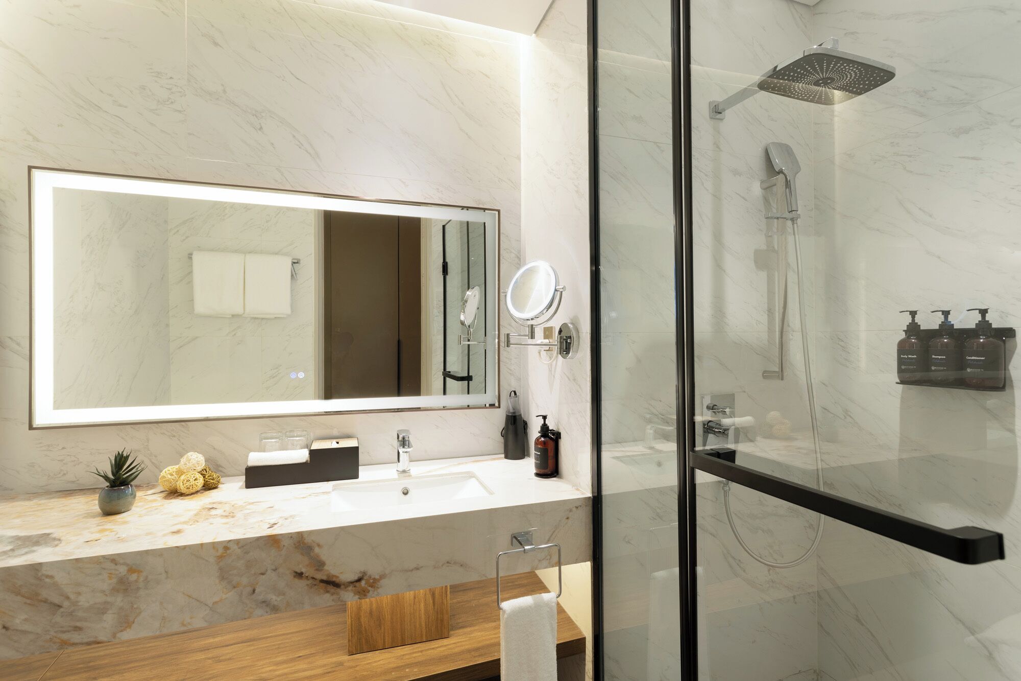 A modern bathroom with a large mirror, a glass-enclosed shower, and a marble countertop.