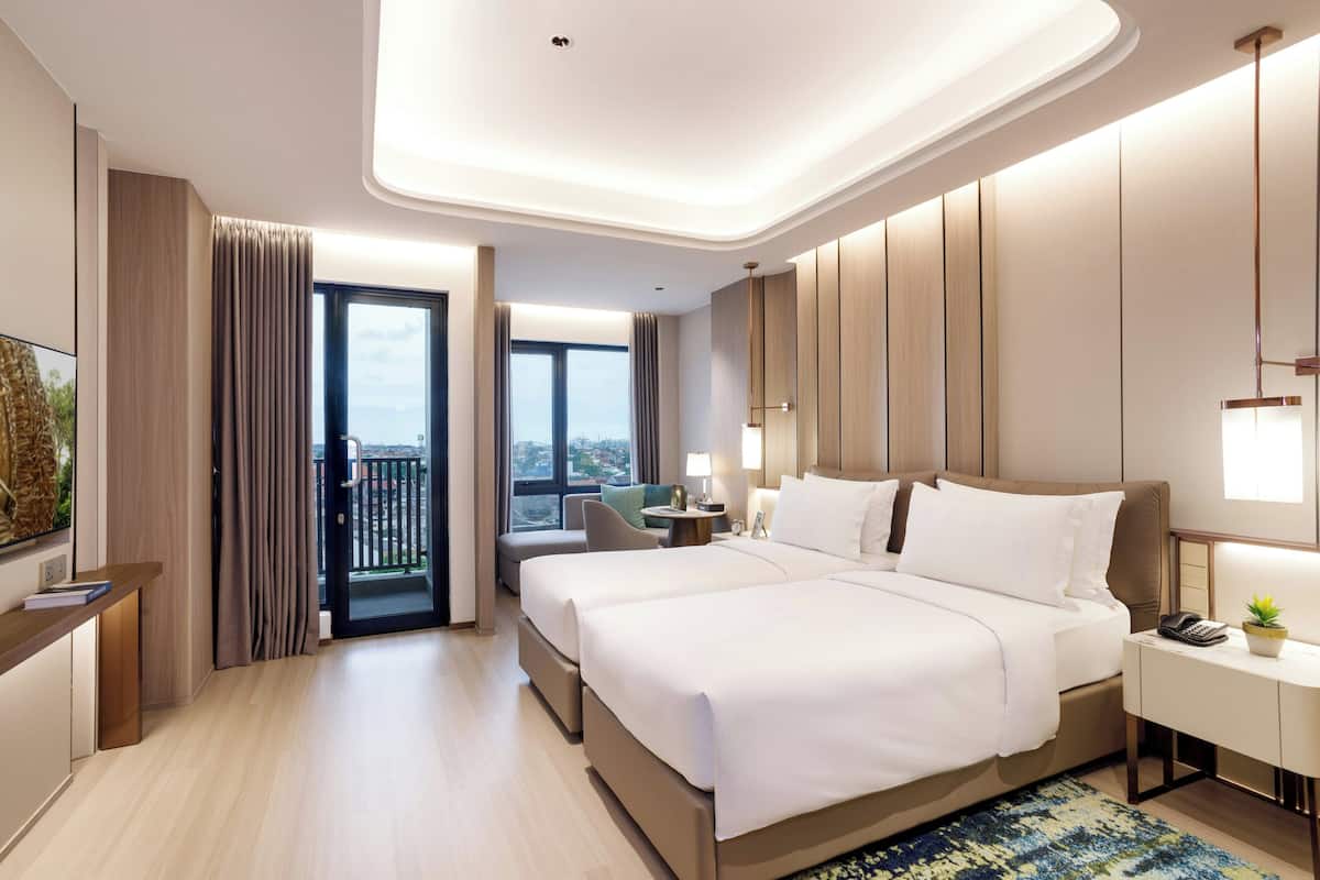 Une chambre d’hôtel moderne dotée d’un grand lit, d’un bureau, d’une chaise, d’une télévision et d’un balcon offrant une vue sur la ville.
