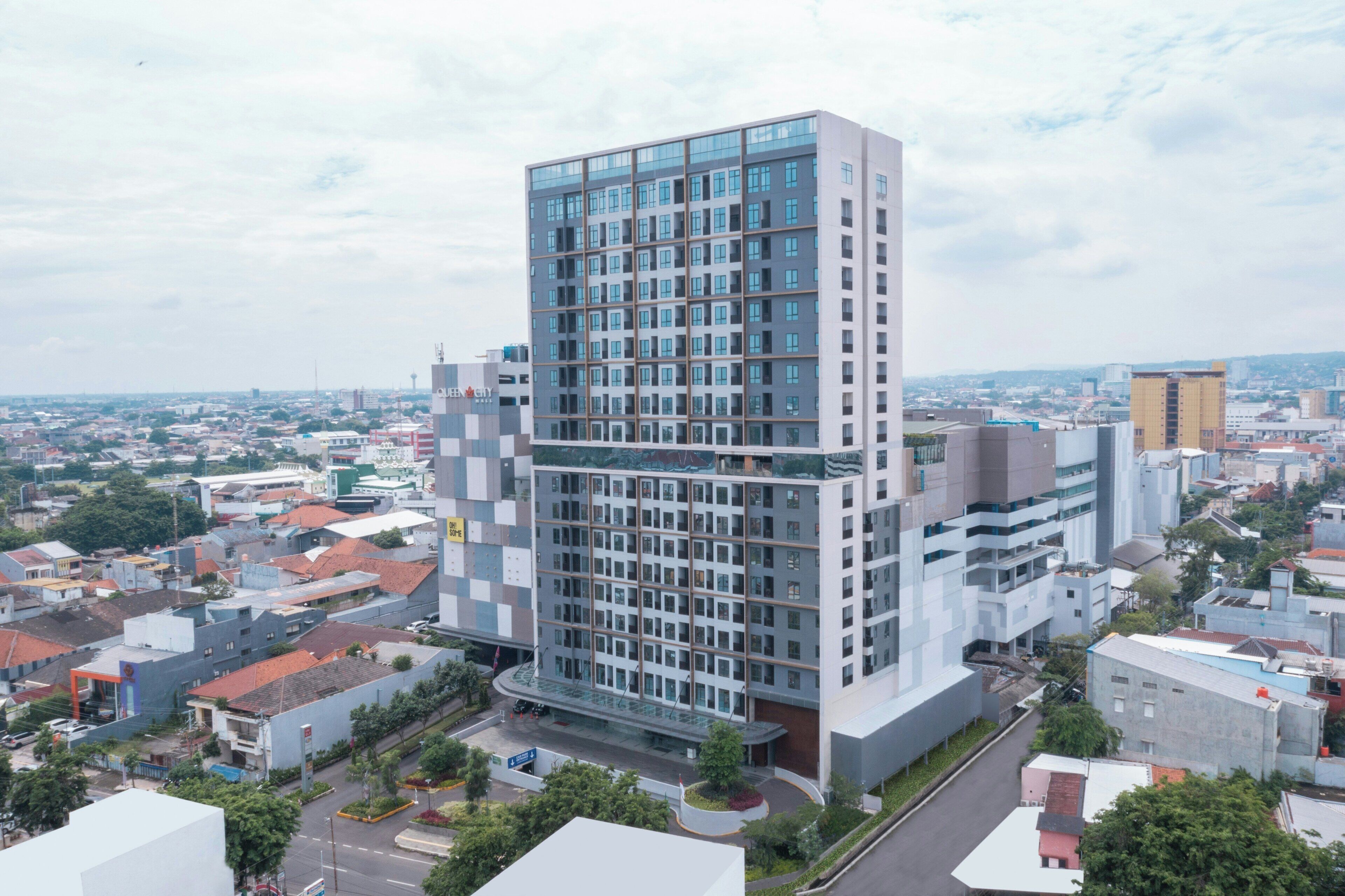 A modern high-rise building with a glass facade, surrounded by a mix of residential and commercial buildings.