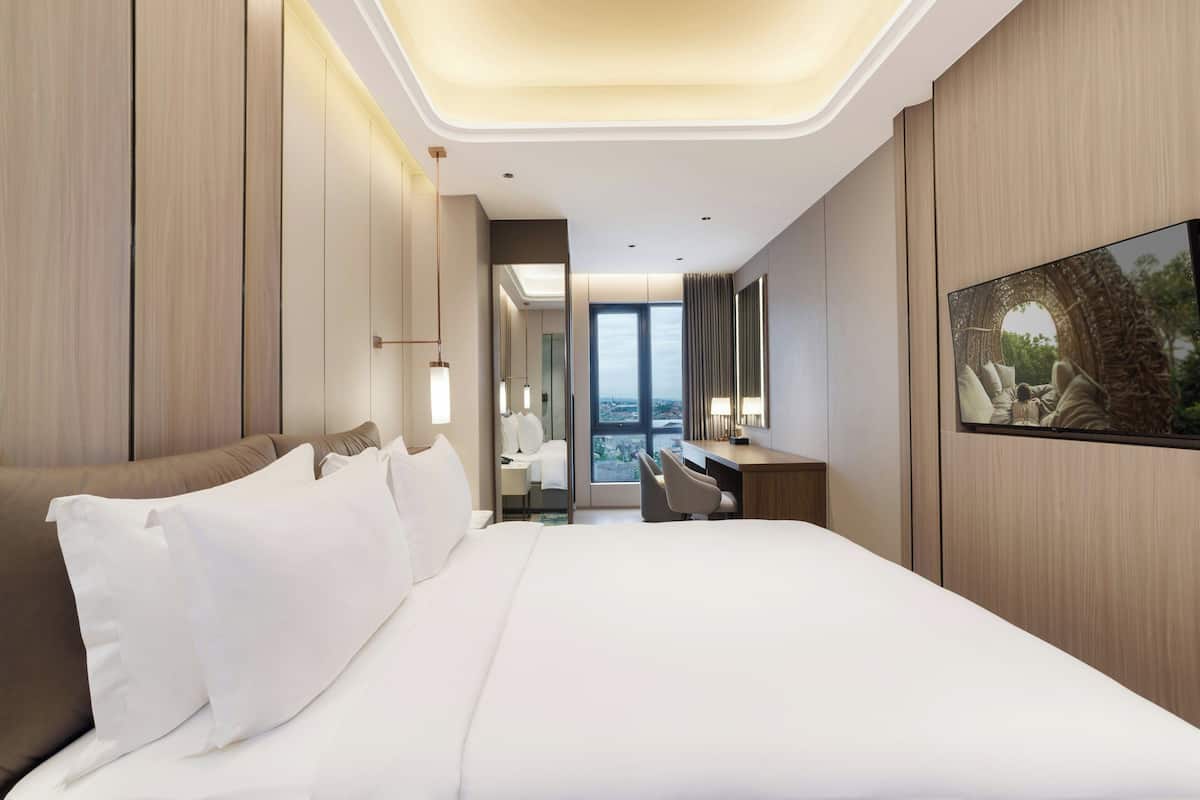 Une chambre d’hôtel moderne, dotée d’un grand lit, d’un bureau et offrant une vue dégagée grâce à une grande fenêtre.