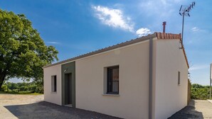 Un pequeño edificio de una sola planta con techo plano y chimenea. Tiene dos ventanas, una puerta y está rodeado de grava.