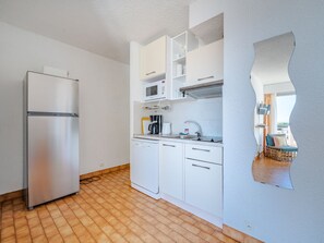 A compact kitchen with a stainless steel refrigerator, white cabinetry, a dishwasher, and a microwave.