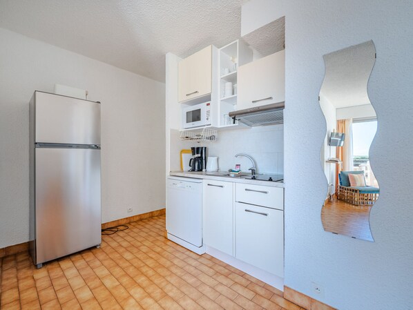 Una cocina compacta con un refrigerador de acero inoxidable, gabinetes blancos, lavavajillas y microondas.
