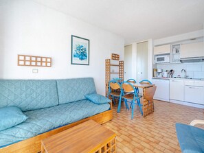 Ein gemütlicher Wohnraum mit einer Couch, einem Esstisch mit Stühlen, einer Küchenzeile inklusive Mikrowelle und einem gerahmten Bild an der Wand.