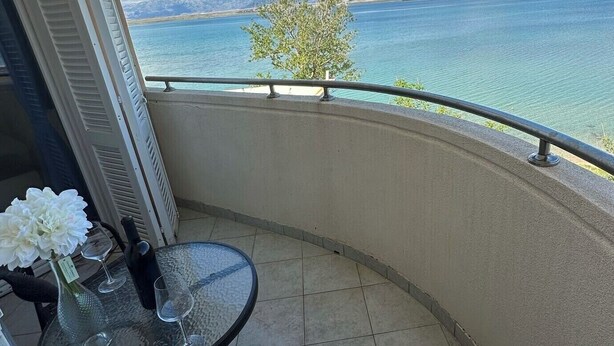 Een balkon met een glazen tafel en stoelen, met uitzicht op een waterpartij en bergen.