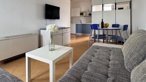 Een moderne woonkamer met een grijze bank, een witte salontafel en een flatscreen televisie aan de muur.