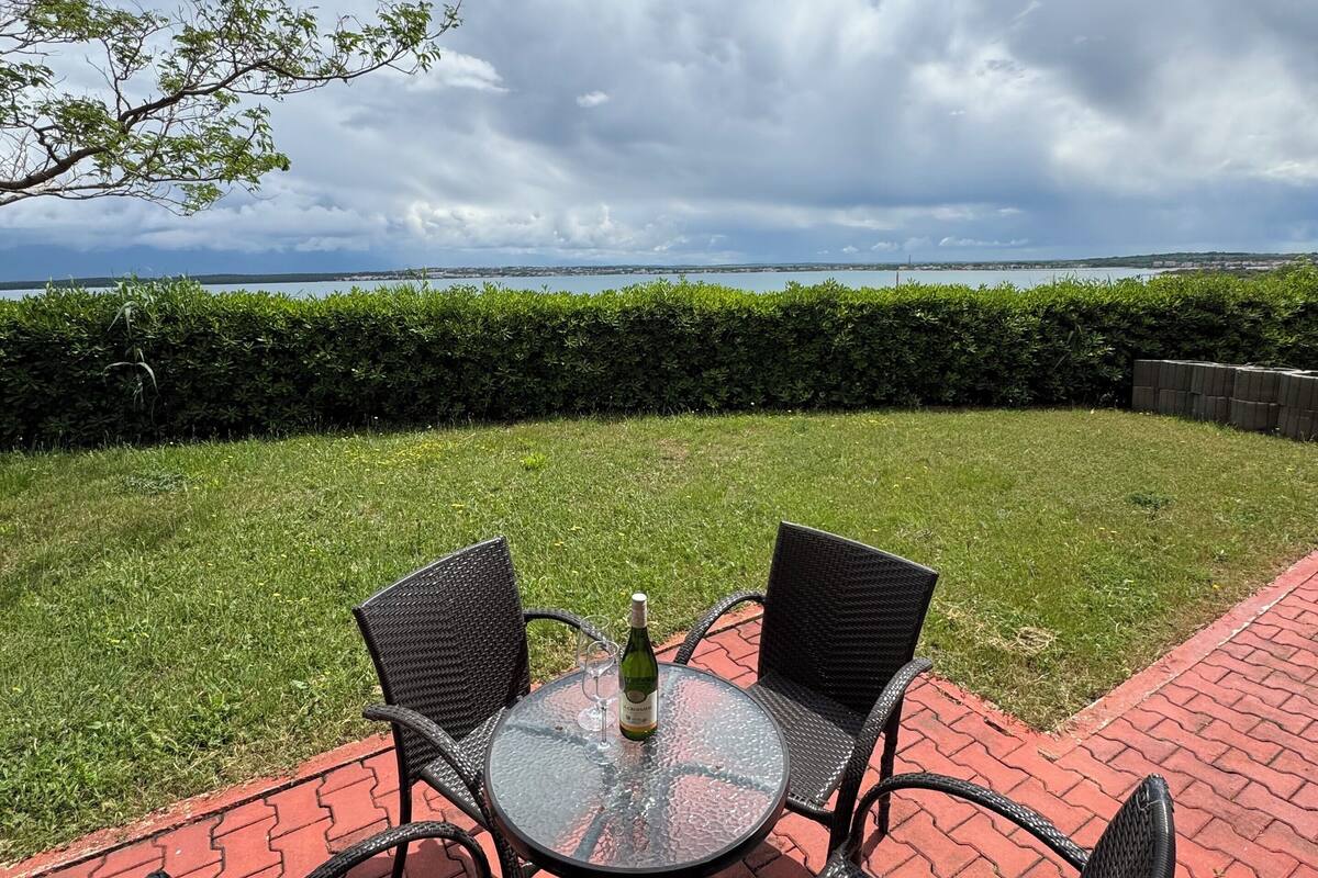 An outdoor patio with a round glass table and four chairs, a bottle of wine, and a glass on the table.