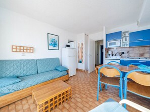 Un espace de vie compact comprenant un coin cuisine, un canapé, une table à manger avec des chaises et un petit banc en bois.