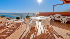 Um terraço com mesa e cadeiras, vista para o mar e chão de azulejos.